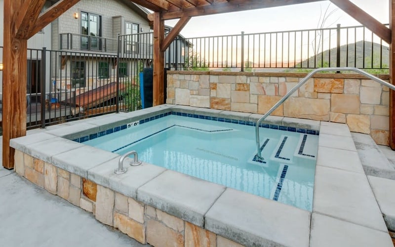 Indoor heated pool with stone surround and wooden beam ceiling, mountain views beyond railing