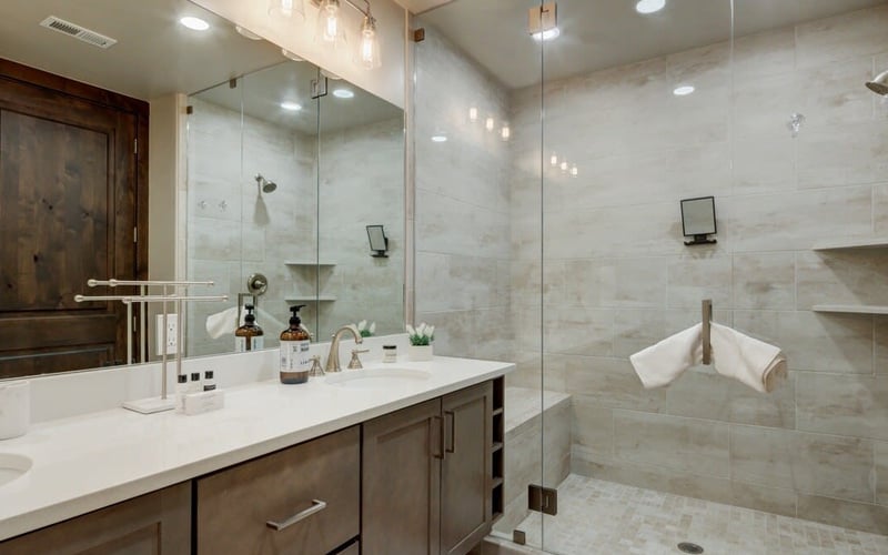 Modern bathroom with marble tile shower, glass enclosure, dark wood vanity, white countertop, and pendant lighting