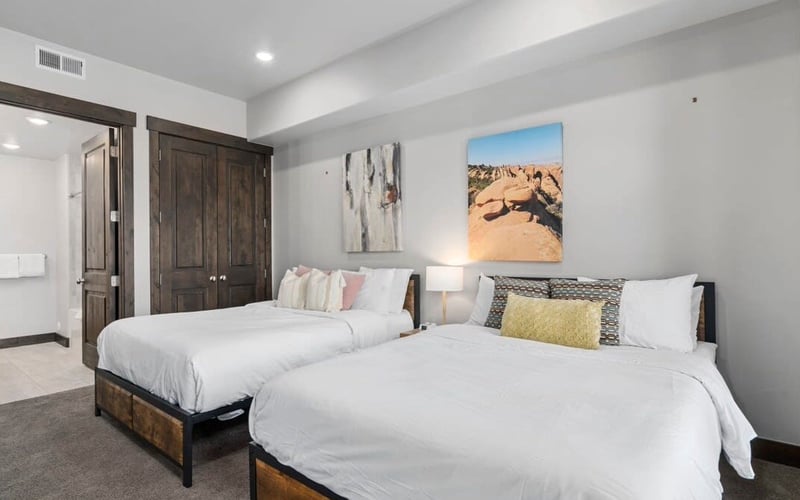Bedroom with two queen beds, white bedding, desert landscape artwork, and dark wood closet doors