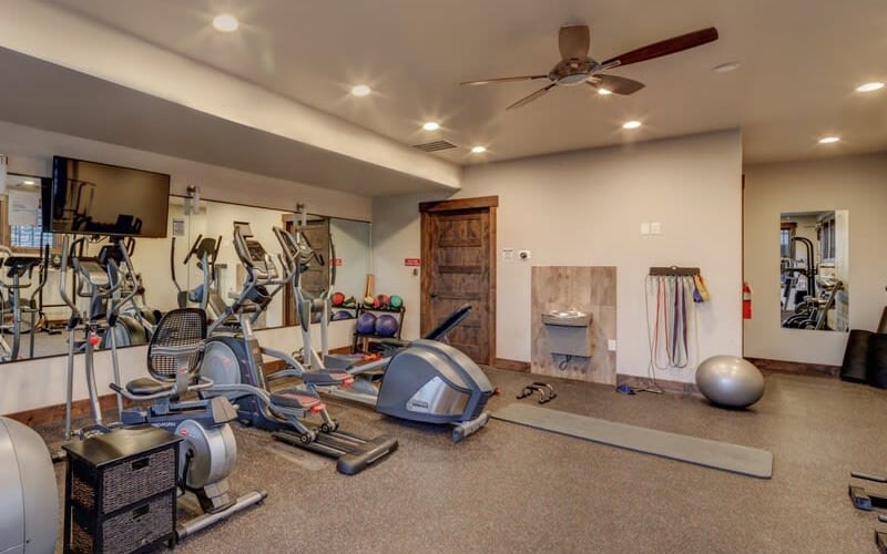 Fitness center with cardio equipment, exercise bikes, ellipticals, yoga mat, stability ball, and wall-mounted workout posters