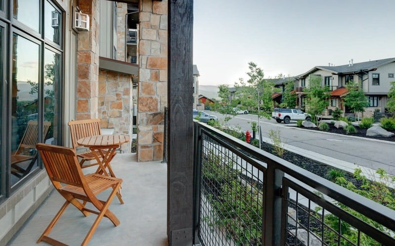 Stone and wood balcony with wooden chairs overlooking residential complex and mountains