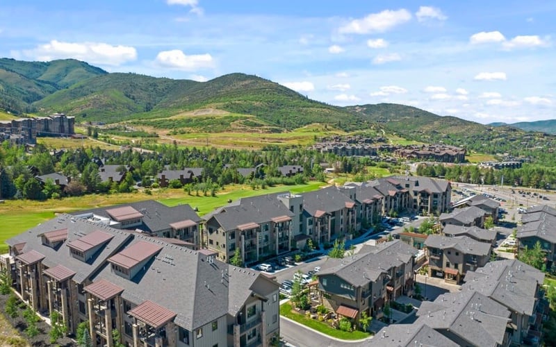 Aerial view of residential complex with multi-story buildings, green courtyards, and mountains in background
