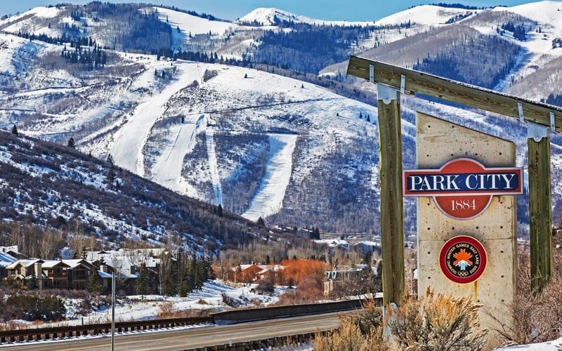 Park City welcome sign with snow-covered ski slopes and mountains in background