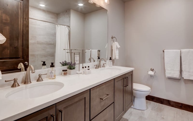 Modern bathroom with dual vanity, white countertop, dark wood cabinetry, large mirror, and walk-in shower with glass enclosure