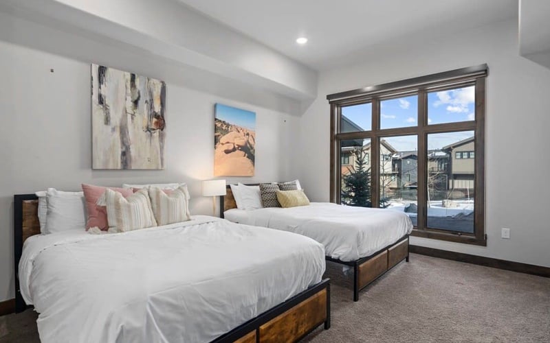 Bright bedroom with two queen beds, large windows overlooking snowy landscape, and framed artwork on white walls