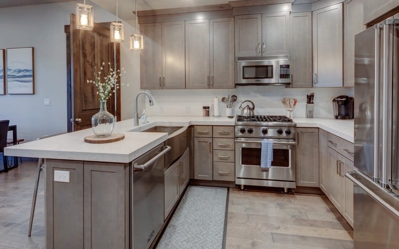 Modern kitchen with gray cabinetry, white quartz countertops, stainless steel appliances, island with pendant lights, and white subway tile backsplash.