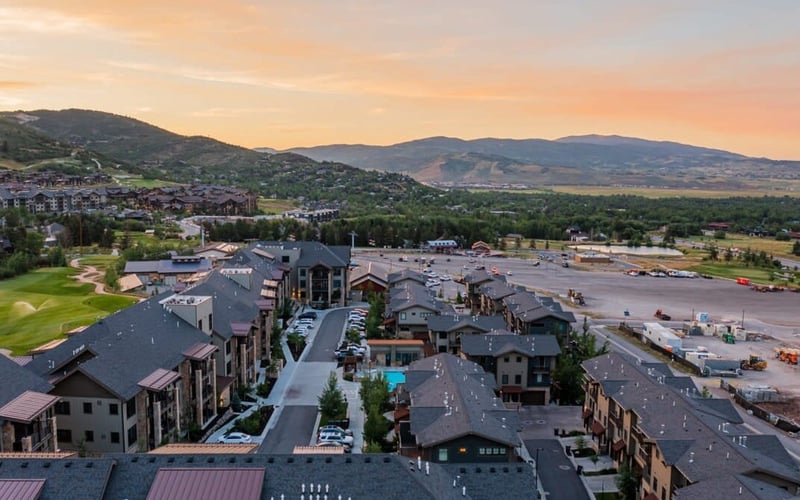 Aerial view of mountain resort with multi-story buildings, parking lot, and valley landscape at sunset