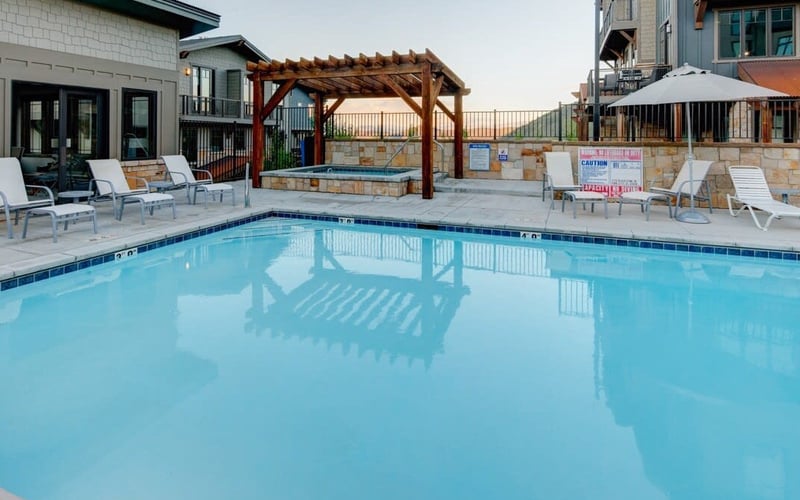 Resort swimming pool with lounge chairs, pergola, hot tub, and residential buildings in background