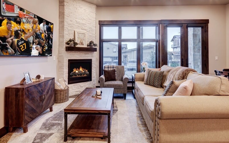 Modern living room with beige sofa, fireplace, large windows overlooking city, and basketball poster on wall